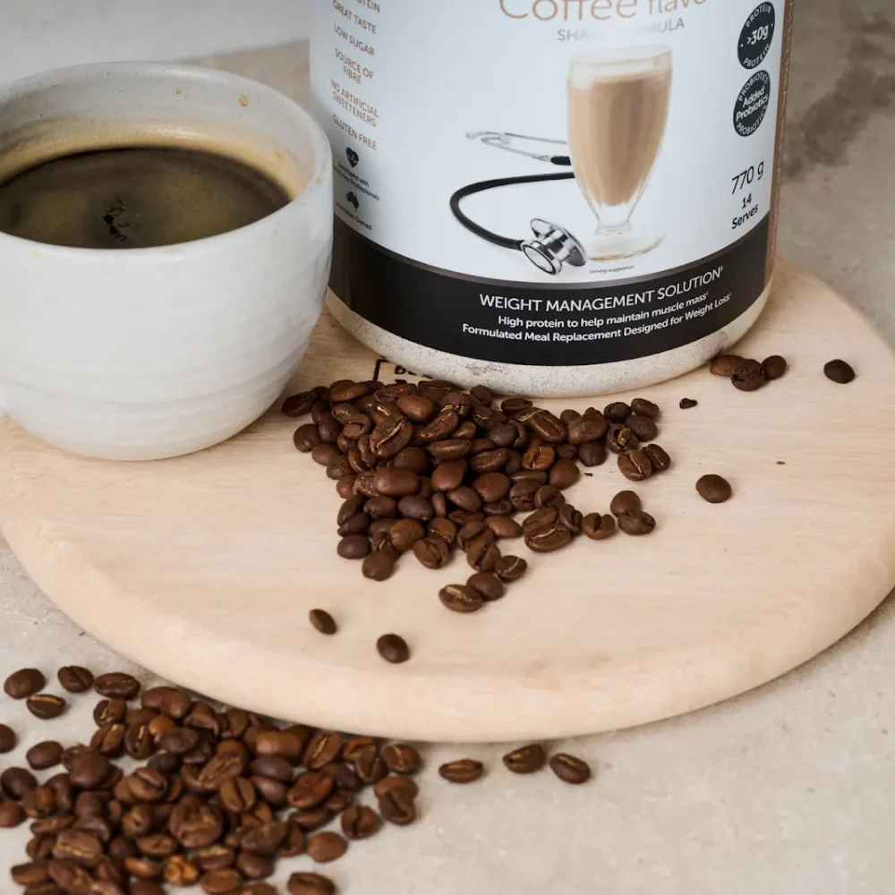 Coffee cup, shake mix, and beans on wooden board. A glass of coffee drink sits nearby.