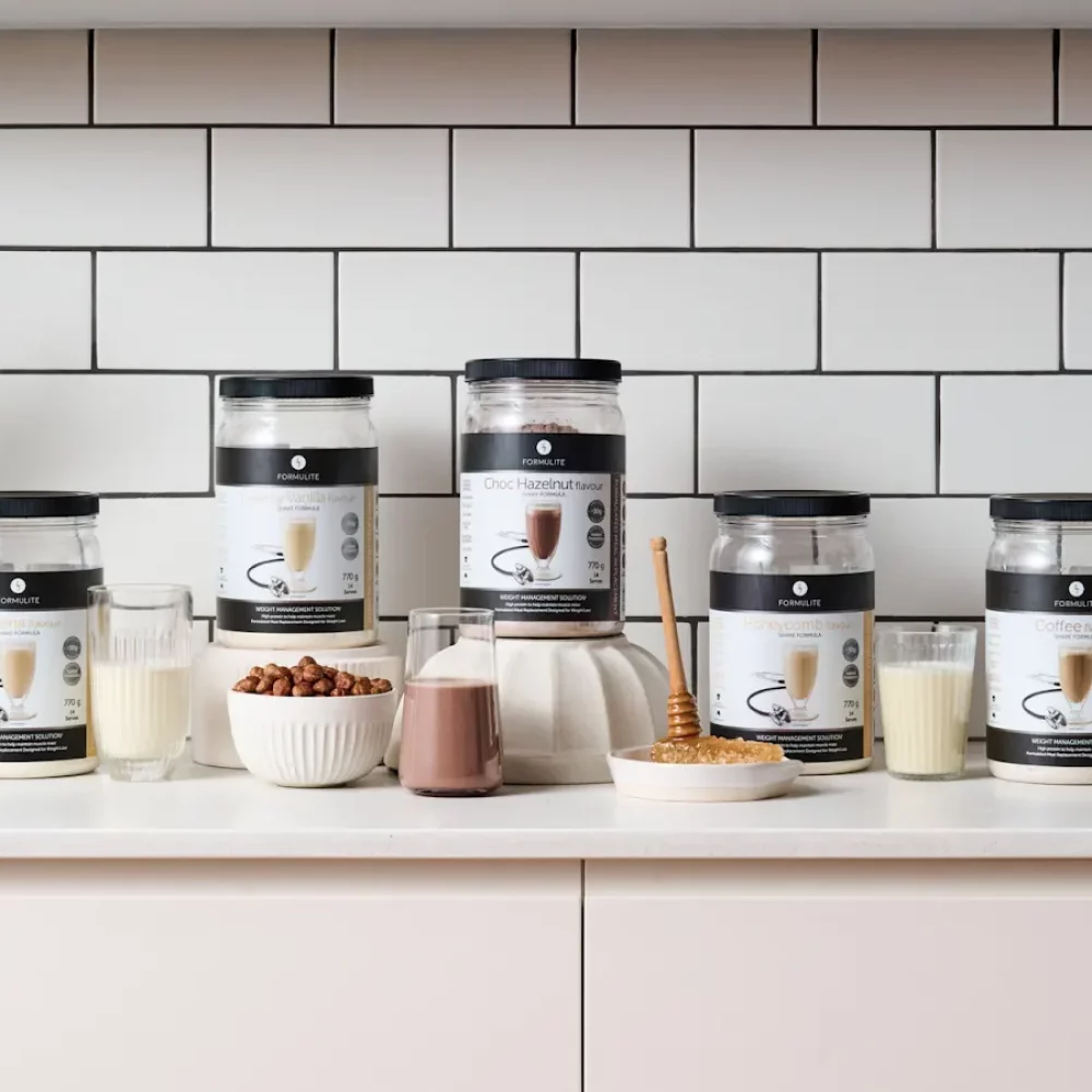 Formulite protein powder jars and prepared drinks on a white counter against a tiled backsplash.