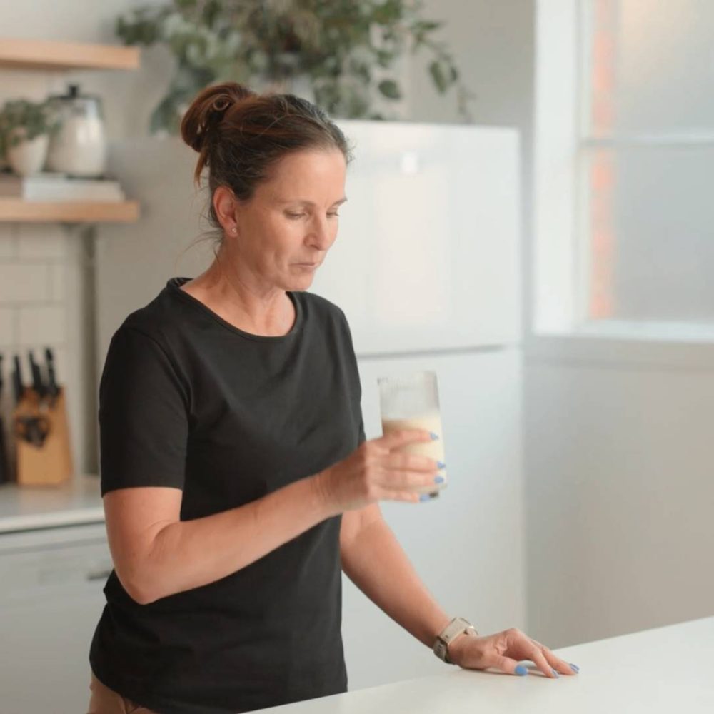 Woman in kitchen looks at a glass of milk she is holding.